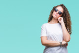 Beautiful brunette curly hair young girl wearing sunglasses over isolated background with hand on chin thinking about question, pensive expression. Smiling with thoughtful face. Doubt concept.