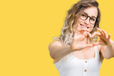 Beautiful young blonde woman wearing glasses over isolated background smiling in love showing heart symbol and shape with hands. Romantic concept.