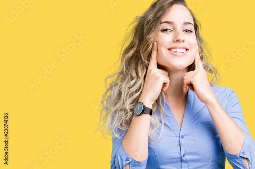 Beautiful young blonde business woman over isolated background Smiling with open mouth, fingers pointing and forcing cheerful smile