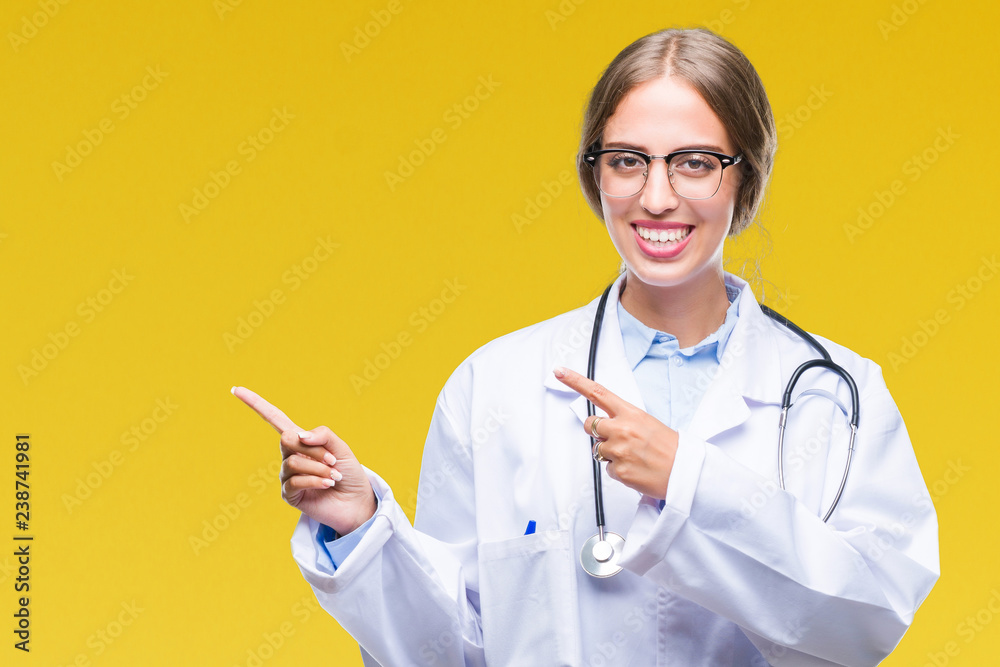 Beautiful young blonde doctor woman wearing medical uniform over isolated background smiling and looking at the camera pointing with two hands and fingers to the side. Beautiful young blonde doctor woman wearing medical uniform over isolated background smiling and looking at the camera pointing with two hands and fingers to the side.