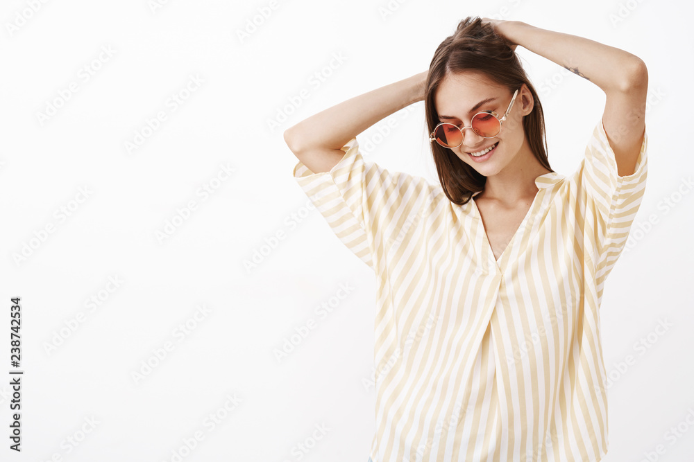 Building her own style. Portrait of charming creative and stylish young female brunette in awesome sunglasses making haircut with hands on back gazing down with broad smile posing in summer clothes Building her own style. Portrait of charming creative and stylish young female brunette in awesome sunglasses making haircut with hands on back gazing down with broad smile posing in summer clothes