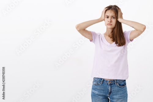 Mind goes round from problems. Portrait of concerned fed up and troubled woman in casual t-shirt holding hands on head looking upset and exhausted being in troublesome situation against grey wall