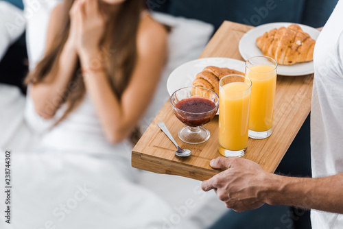 cropped view of man holding wooden tray with orange juice and croissants