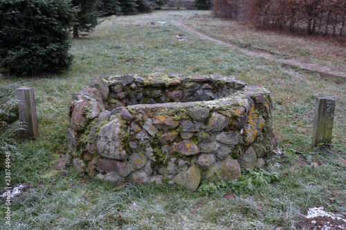 Old hidden manhole from the cobblestones among the grass and dry fallen leaves photo