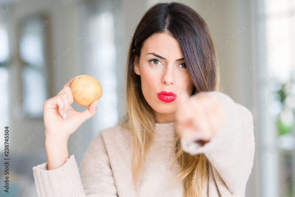 Young beautiful woman holding fresh potato at home pointing with finger to the camera and to you, hand sign, positive and confident gesture from the front Young beautiful woman holding fresh potato at home pointing with finger to the camera and to you, hand sign, positive and confident gesture from the front