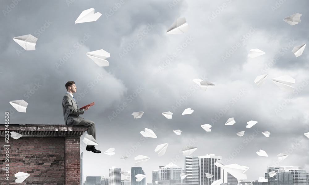 Man on roof edge reading book and cityscape at background Man on roof edge reading book and cityscape at background