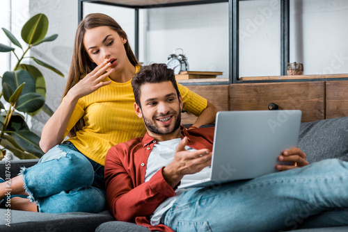young surprised couple sitting on sofa and using laptop