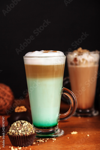 Coffee latte macchiato with mint syrup and whipped cream  in high transparent glasses  on a wooden table  on a dark background with cakes
