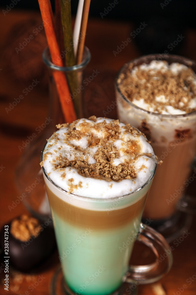 Coffee latte macchiato with mint syrup and whipped cream, sprinkled with chopped halva, in high transparent glasses, on a wooden table Coffee latte macchiato with mint syrup and whipped cream, sprinkled with chopped halva, in high transparent glasses, on a wooden table