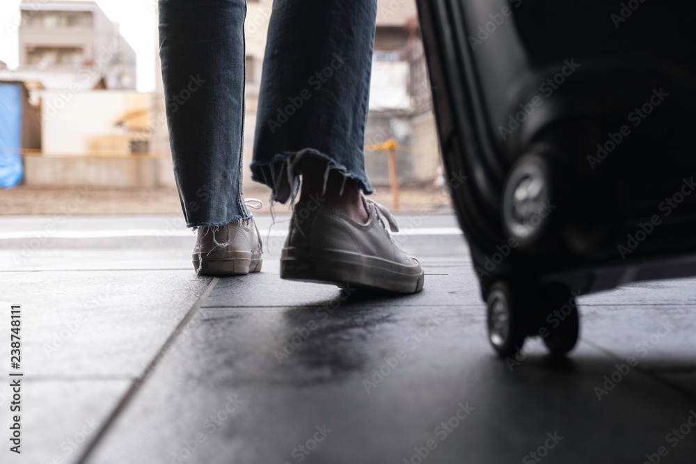 Closeup image of a woman's feet while traveling and dragging a black baggage in the outdoors Closeup image of a woman's feet while traveling and dragging a black baggage in the outdoors