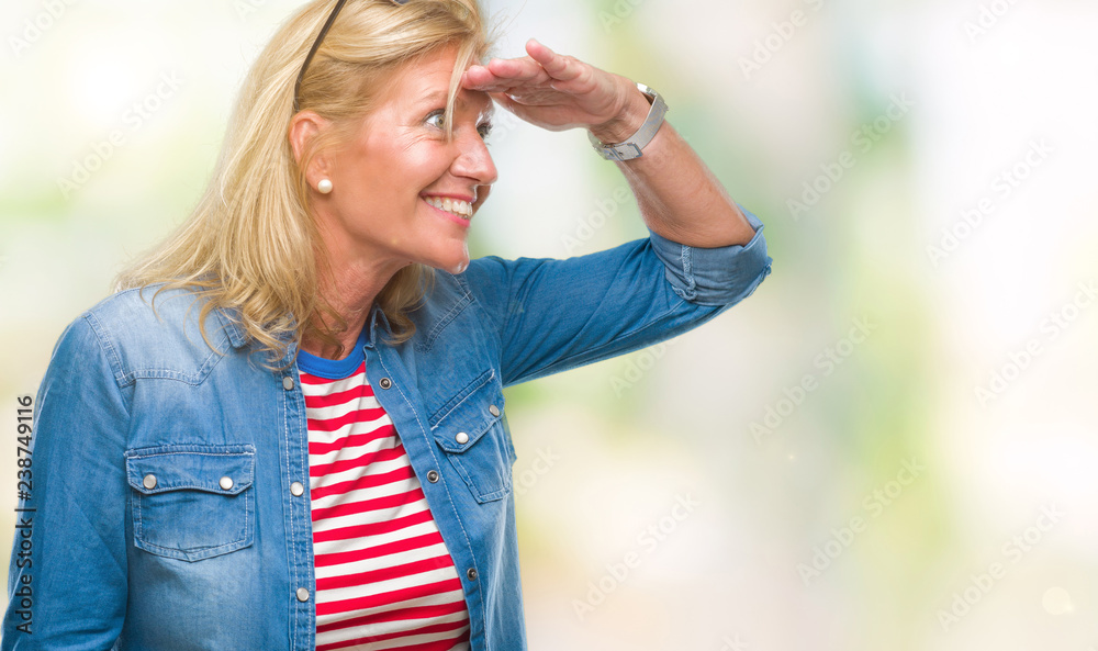 Middle age blonde woman over isolated background very happy and smiling looking far away with hand over head. Searching concept.