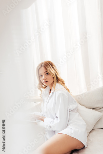 selective focus of pretty young woman with blonde hair looking at camera in bed