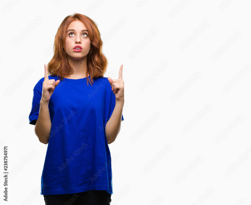 Young beautiful woman over isolated background amazed and surprised looking up and pointing with fingers and raised arms. Young beautiful woman over isolated background amazed and surprised looking up and pointing with fingers and raised arms.