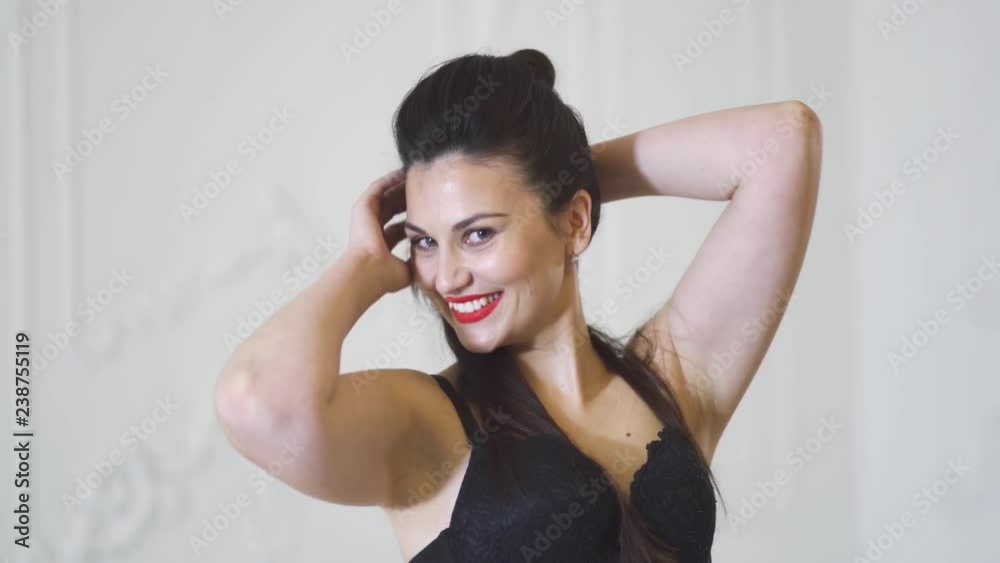 Beautiful smiling girl in black bra posing on a white background in the studio. Cute girl in lingerie posing in bright studio. Charming woman smiles and straightens hair. Beautiful smiling girl in black bra posing on a white background in the studio. Cute girl in lingerie posing in bright studio. Charming woman smiles and straightens hair.