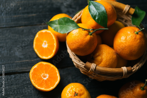 Juicy bright ripe tangerines in wooden basket on dark background