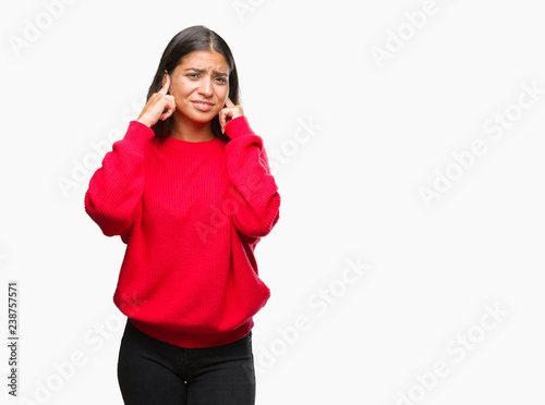 Young beautiful arab woman wearing winter sweater over isolated background covering ears with fingers with annoyed expression for the noise of loud music. Deaf concept.