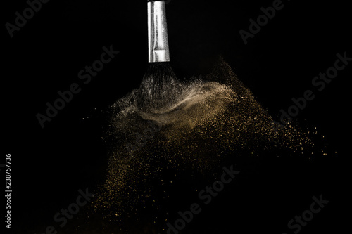 gold powder splash and brush for makeup artist or graphic design in black background, look like a luxury mood