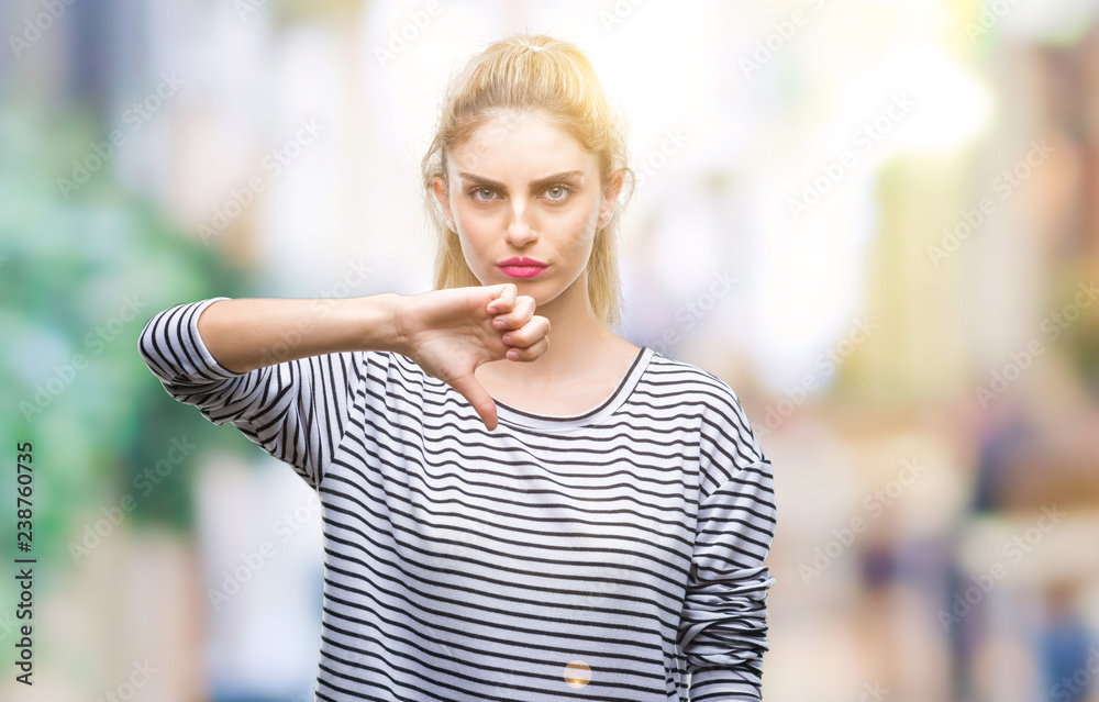 Young beautiful blonde woman wearing stripes sweater over isolated background looking unhappy and angry showing rejection and negative with thumbs down gesture. Bad expression.