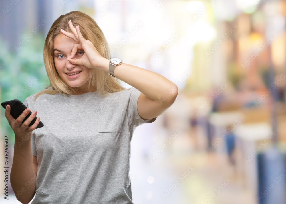 Young caucasian woman sending message using smartphone over isolated background with happy face smiling doing ok sign with hand on eye looking through fingers