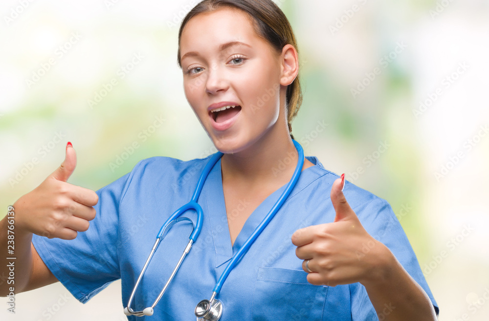 Young caucasian doctor woman wearing medical uniform over isolated background approving doing positive gesture with hand, thumbs up smiling and happy for success. Looking at the camera Young caucasian doctor woman wearing medical uniform over isolated background approving doing positive gesture with hand, thumbs up smiling and happy for success. Looking at the camera