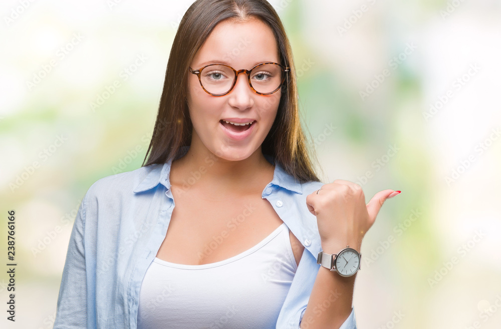 Young caucasian beautiful business woman wearing glasses over isolated background smiling with happy face looking and pointing to the side with thumb up. Young caucasian beautiful business woman wearing glasses over isolated background smiling with happy face looking and pointing to the side with thumb up.