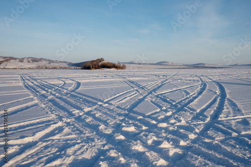 Car tracks go across the frozen Great Lake to the island against the backdrop of the village of Parnaya, Krasnoyarsk Territory. Russia. photo