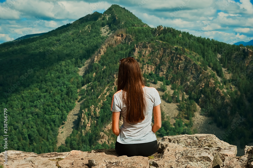 A young girl in the mountains sits back.