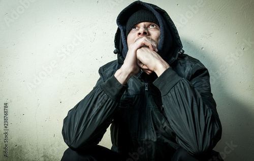 Homeless man drug and alcohol addict sitting alone and depressed on the street in winter clothes feeling anxious cold and lonely, social documentary concept dramatic image