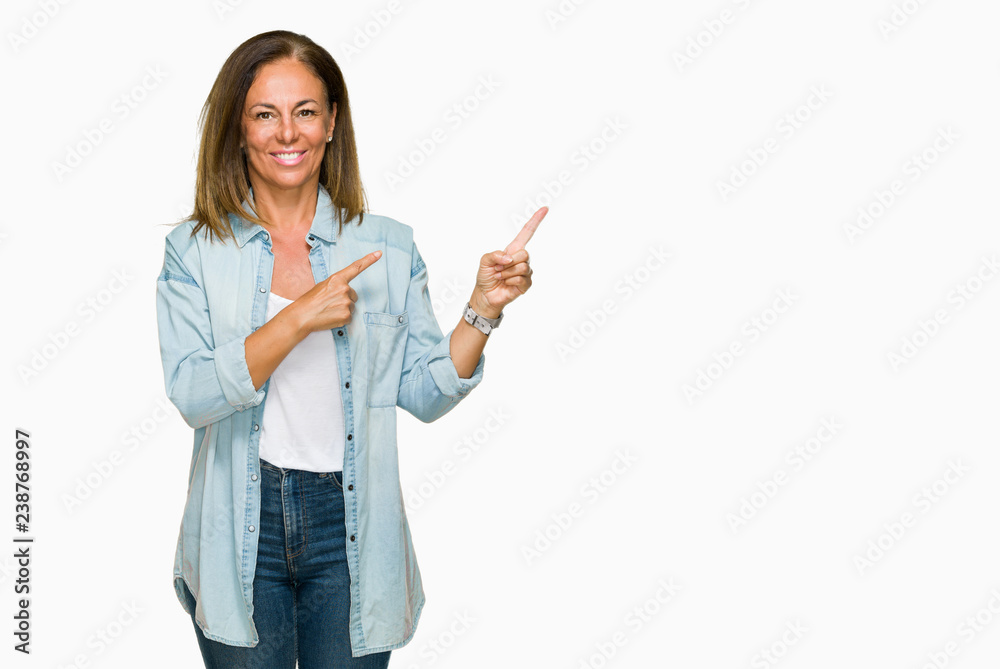 Middle age adult woman wearing casual denim shirt over isolated background with a big smile on face, pointing with hand and finger to the side looking at the camera. Middle age adult woman wearing casual denim shirt over isolated background with a big smile on face, pointing with hand and finger to the side looking at the camera.