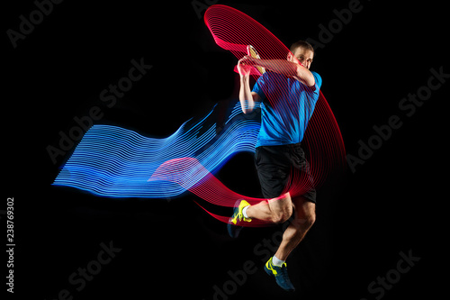 The one caucasian man playing tennis isolated on black background. Studio shot of fit young player at studio in motion or movement during sport game with led light trail © master1305