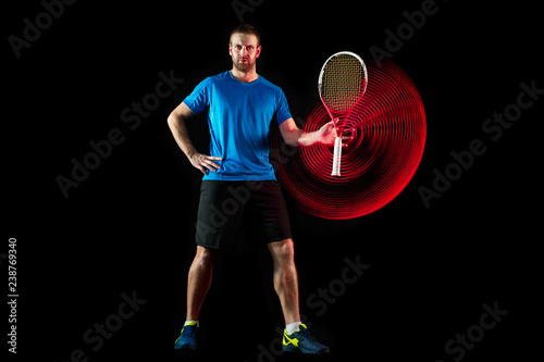 The one caucasian man playing tennis isolated on black background. Studio shot of fit young player at studio in motion or movement during sport game with led light trail