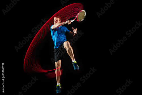 The one caucasian man playing tennis isolated on black background. Studio shot of fit young player at studio in motion or movement during sport game with led light trail © master1305