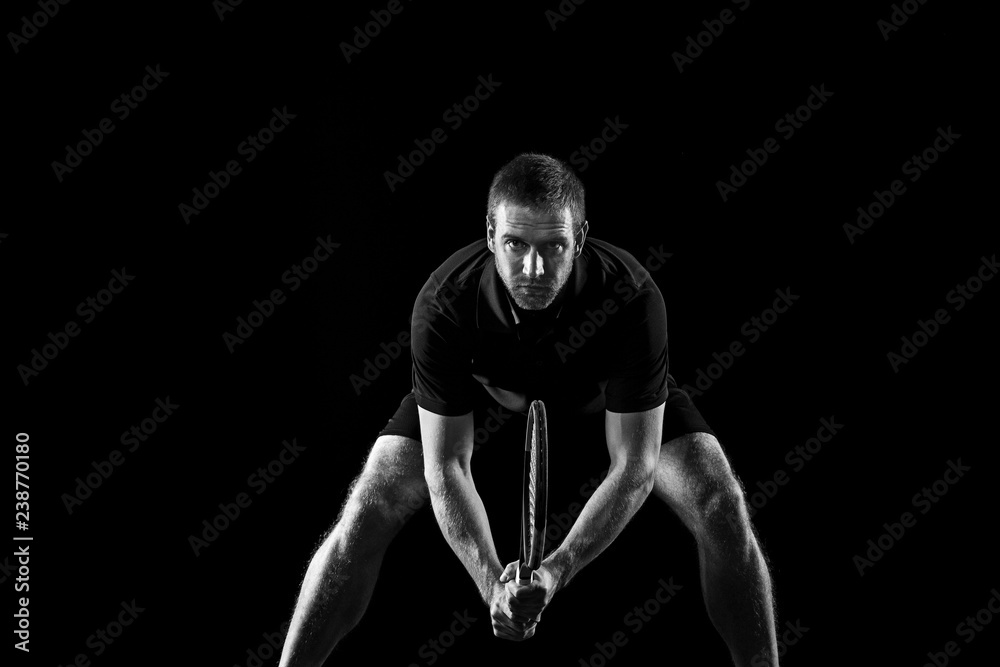 The one caucasian man playing tennis isolated on black background. Studio monochrome shot of fit young player at studio in motion or movement during sport game.. The one caucasian man playing tennis isolated on black background. Studio monochrome shot of fit young player at studio in motion or movement during sport game..