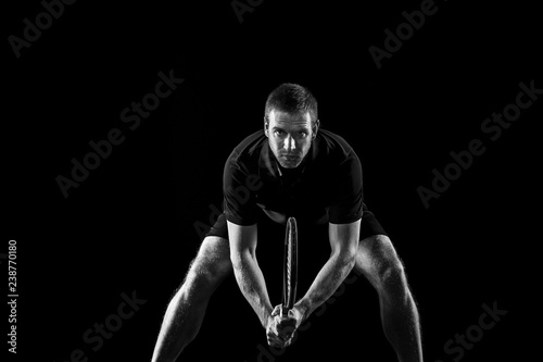 The one caucasian man playing tennis isolated on black background. Studio monochrome shot of fit young player at studio in motion or movement during sport game.. © master1305