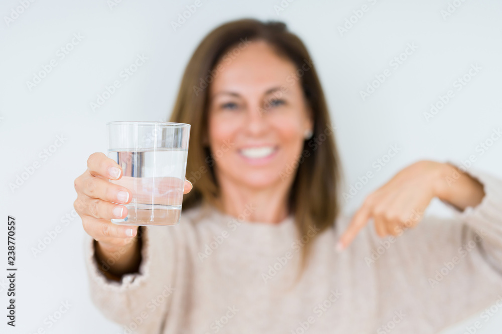 Middle age woman drinking glass of water isolated background with surprise face pointing finger to himself Middle age woman drinking glass of water isolated background with surprise face pointing finger to himself