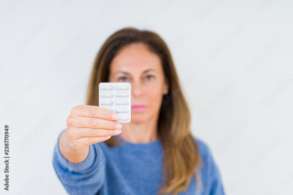 Middle age woman holding pharmaceutical pills over isolated background with a confident expression on smart face thinking serious Middle age woman holding pharmaceutical pills over isolated background with a confident expression on smart face thinking serious