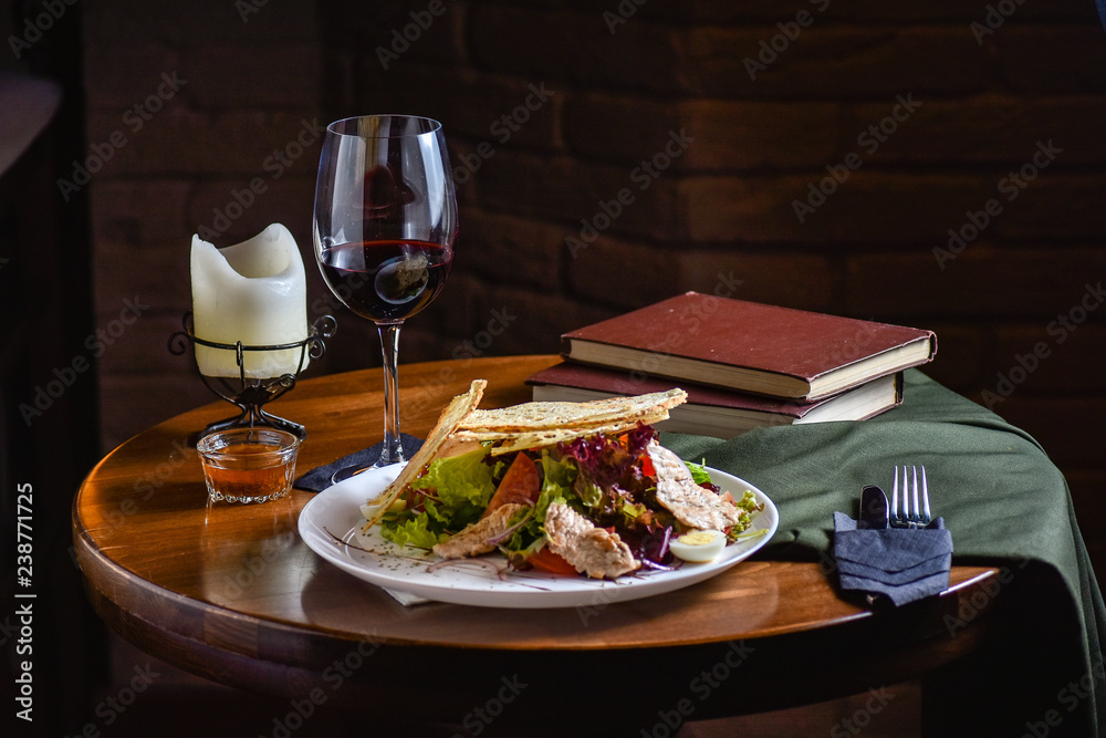 Fresh and tasty salad and red vine on the table. Food still life, home cooking recipe. Natural light, slightly toned image, dark black background with text area. Horizontal view.