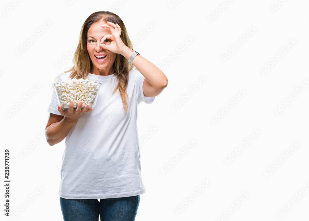 Middle age hispanic woman eating popcorn over isolated background with happy face smiling doing ok sign with hand on eye looking through fingers