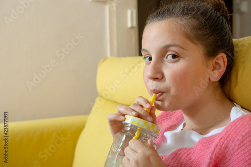 young teenage girl sitting in a yellow sofa drinking orange juice