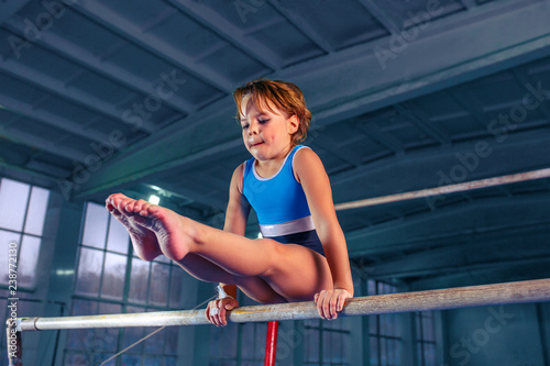 Fotografie The beautiful little girl is engaged in sports gymnastics on a parallel bars at gym