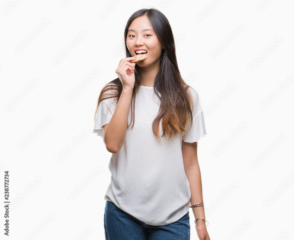 Young asian woman eating chocolate chip cookie over isolated background with a confident expression on smart face thinking serious Young asian woman eating chocolate chip cookie over isolated background with a confident expression on smart face thinking serious