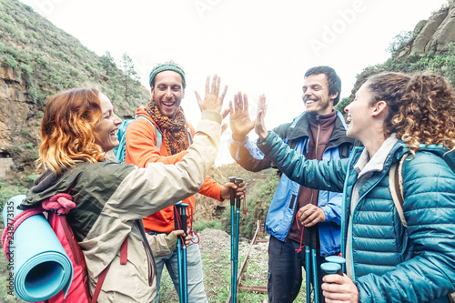 Group of friends stacking hands while doing trekking excursion on mountain - Young  tourists walking and exploring the wild nature - Trekker, team, hike and travel people concept