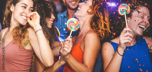 Happy friends doing party dancing in the nightclub - Trendy young people having fun celebrating together with confetti and candy lollipops in disco - Entertainment, youth lifestyle holidays concept