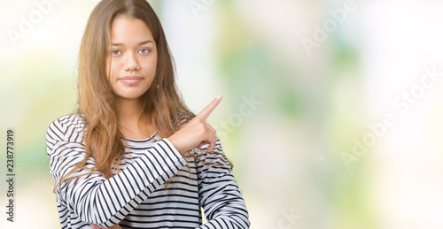 Young beautiful brunette woman wearing stripes sweater over isolated background Pointing with hand finger to the side showing advertisement, serious and calm face © Krakenimages.com