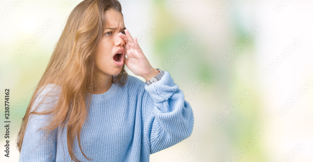Young beautiful brunette woman wearing blue winter sweater over isolated background shouting and screaming loud to side with hand on mouth. Communication concept.