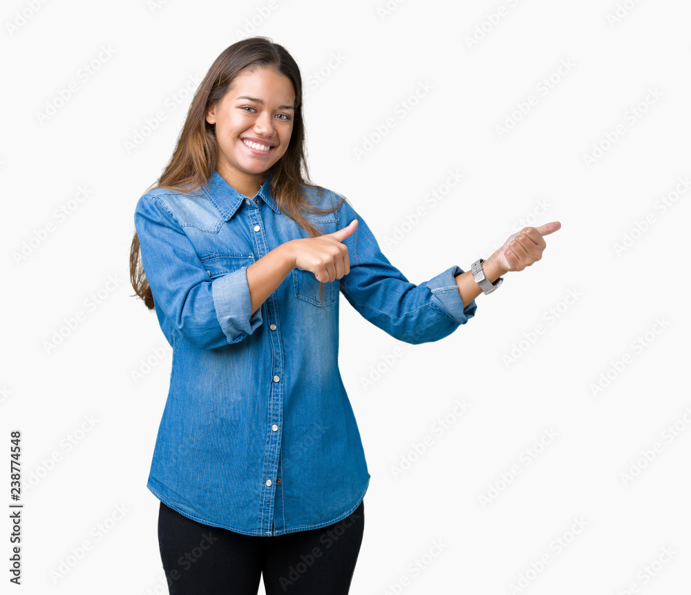 Young beautiful brunette woman wearing blue denim shirt over isolated background Pointing to the back behind with hand and thumbs up, smiling confident Young beautiful brunette woman wearing blue denim shirt over isolated background Pointing to the back behind with hand and thumbs up, smiling confident