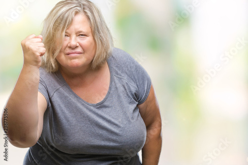 Senior plus size caucasian woman over isolated background angry and mad raising fist frustrated and furious while shouting with anger. Rage and aggressive concept.