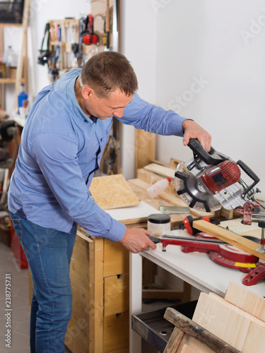 Woodworker male cutting wooden plank with fret saw in workplace