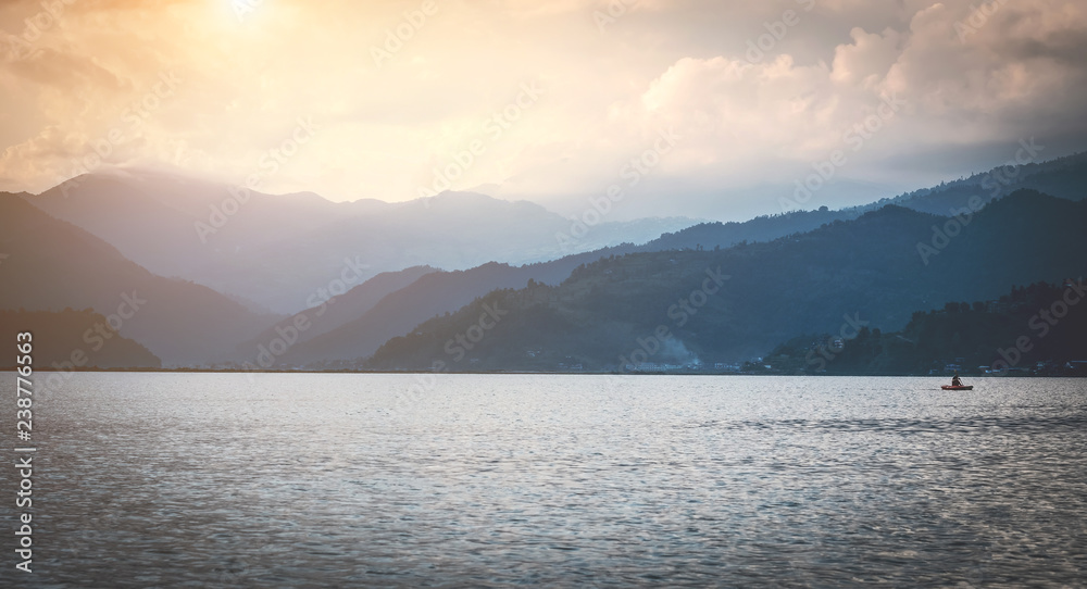 View on Phewa lake surrounded by mountains in light fog in the evening, Pokhara, Nepal.