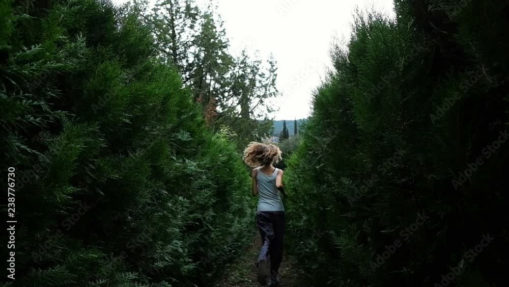 Curly woman runs away into the spruce and fluffy bushes, slow motion Curly woman runs away into the spruce and fluffy bushes, slow motion